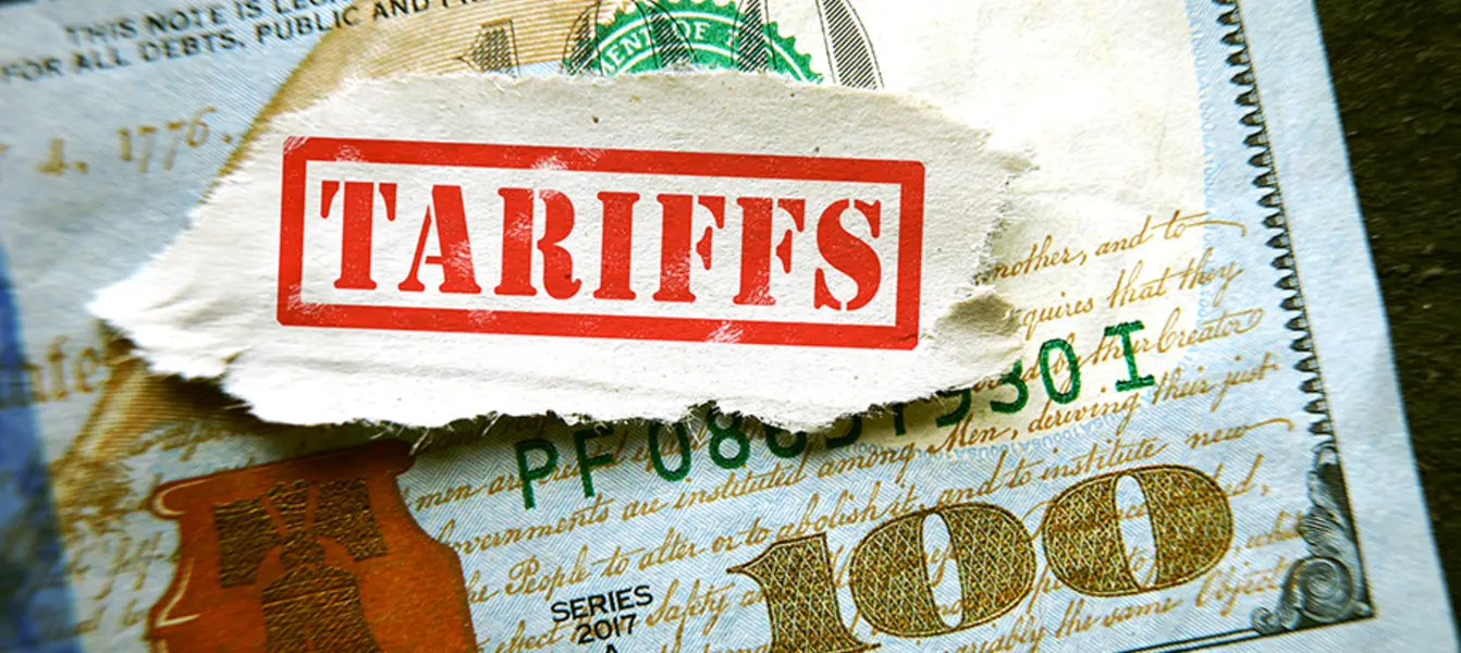 A US one hundred dollar bill beneath a banner that says "TARIFFS"