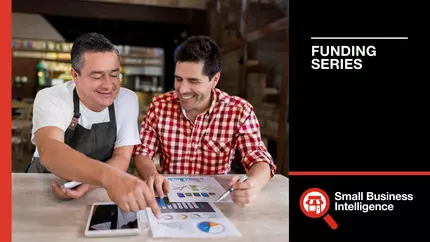 Two male business owners, smiling, reviewing credit history for their small company.