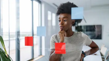 Entrepreneur looking at clear memo board with red post-its trying to figure out his next steps.