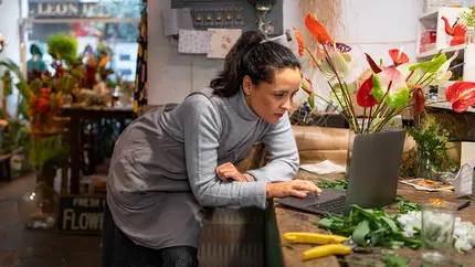 small business owner staring at laptop in her flower shop, figuring out a mistake and correcting.